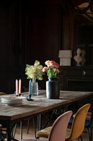 Flowers on large wooden dining table in dark dining room 