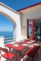 Outdoor dining table laid for lunch on red and white terrace with sea views 
