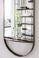 Cut flowers in glass vases on mirror ledge with reflection of modern shelving 