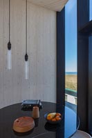 Small circular table and bare pendant lighting next to window with coastal view