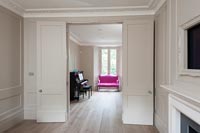 View of piano and bright pink sofa through panelled double doors 