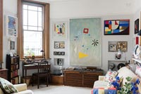 Modern living room with colourful artwork on walls and desk by window 