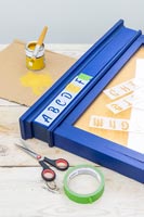 Letter stencils - painting onto blue wooden frame of notice board 