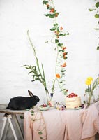 Pet rabbit on garden table filled with flowers and picnic food 
