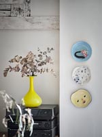 Display of ceramic plates on wall next to yellow vase 