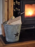 Firewood in metal bucket next to lit wood burning stove 
