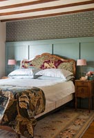 Green panelled wall behind bed with decorative headboard 