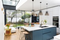 Contemporary modern kitchen in a side return extension with a blue island, wooden floors, light pendants, bar stools and slim frame tall glass doors.