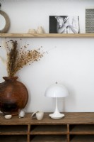 White lamp and wooden vase of dried flowers on wooden unit