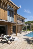 Recliners on decking next to swimming pool - modern wooden house