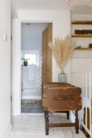 Contemporary white subway tiled bathroom features bath with copper taps, bath rack, pampus grass, steamer trunk, and plant.