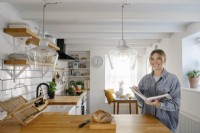 Kati Scalet Stands in her contemporary L-shaped Kitchen with white subway tiles and wooden work surface. Under the window is a L-shaped banquette seating area.
