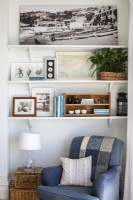 Comfortable blue armchair in alcove, shelves covered with vintage prints and guide books