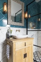 Detail of wooden vanity and sink with brass taps, Moroccan style mirror and bold tiles.