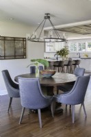 Round wooden dining table and upholstered chairs in modern open plan dining room and kitchen.