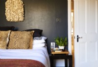 Detail of bed and side table against black painted wall with wall art. 