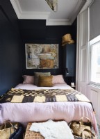 A double bed in a small bedroom with black painted walls and ethnic style fabrics.