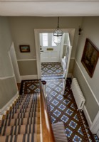 A view of the entrance hall seen from the first floor, showing g decorative tiled floor and striped runner on the stairs. 