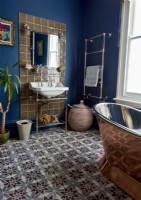 A dark blue bathroom with copper coloured freestanding roll top bath and victorian style sink. 