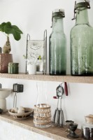 Detail of open wooden kitchen shelves with collections of vintage glass bottles and accessories