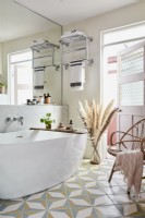 Bathroom with oval bath and tiled floor, mirror wall pink door, wicker armchair