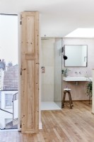 Open plan ensuite bathroom with shower and sink, wooden floor boards and skylight and views over rooftops 