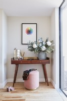 Detail of bedroom dressing table with flowers, contemporary window and framed art. Pouffe on wooden floorboards