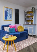 Open-plan seating area with a blue sofa, crockery cupboard and a pink spotty rug.