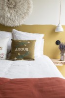 Embroidered cushion on bed with half wall painted mustard behind