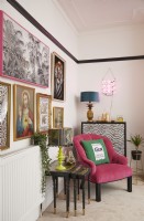 Colourful living room detail with a pink armchair, nest of side tables a gallery wall.
