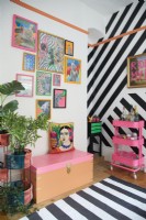 Colourful home office detail with framed artwork, black vinyl striped wall and fluorescent drinks trolley. 