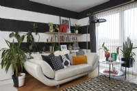 Black and white striped walls in a modern open plan living room space. With a cream leather sofa and patterned rug.