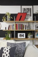 Detail of open bookshelves in a modern open plan living room space with black and white striped walls. With hand painted concrete plant pots.