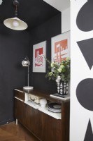 Hallway showing a retro sideboard with hanging graphic artwork above and black and white painted shapes on the walls.