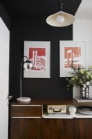 Hallway showing a retro sideboard with hanging graphic artwork above and black and white painted walls.
