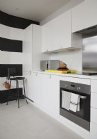 Contemporary kitchen in an open plan living space. With white cabinets and black and white striped walls and a stool.