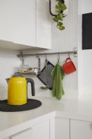 Contemporary kitchen detail showing yellow kettle, hanging utensils and white hexagon tiles.