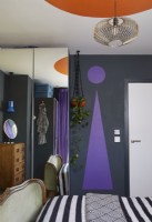 Bold and colourful painted bauhaus shapes in a contemporary bedroom. Showing purple and orange painted shapes with monochrome striped bedding.