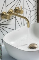 Brass tap with running water into small modern white sink