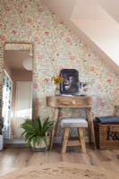 Wooden dressing table next to floral wallpapered wall