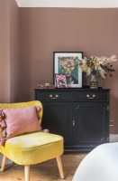 Black cabinet and yellow chair in bedroom with pink painted walls