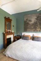 Painting on teal blue painted wall in country bedroom with fireplace