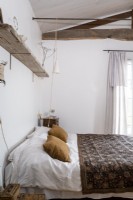 White bedroom with brown bedspread and exposed wooden beams
