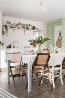 Dining table in open plan pale pink and green kitchen diner with eclectic mix of wooden chairs