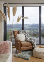 Leather armchair with pampas grass and a countryside view through bifold doors.