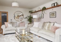 Living room with neutral sofas, a gold coffee table, open shelving and a round mirror.