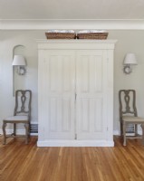 A vintage armoire got a makeover with white paint and is now used to store bed linens, blankets, throws and other necessary items. Symmetry is created with a pair of identical chairs, wall sconces and baskets.