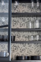Dishes and glassware displayed on shelving lined with wallpaper.