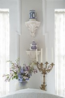 United with white paint, mismatched wall sconces make a fitting stage for displaying a Wedgwood pitcher and transferware canister. 