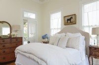 The sunny master bedroom features a new headboard upholstered in tan linen. Antiques, including an oak dresser and polished wood side tables, bring an old-world sense of coziness to the restful space.
